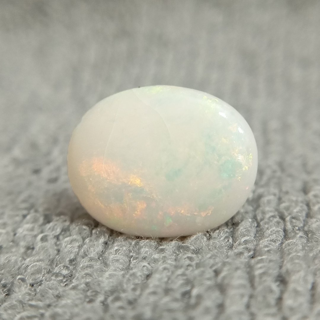 A close-up of a Natural Opal gemstone displaying a mesmerizing play of colors with iridescent flashes.